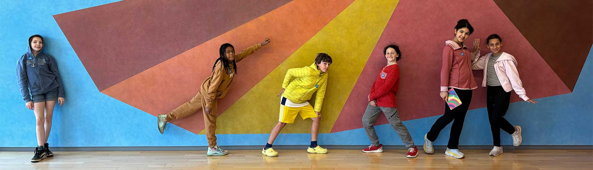 Six students strike poses in front of an art mural